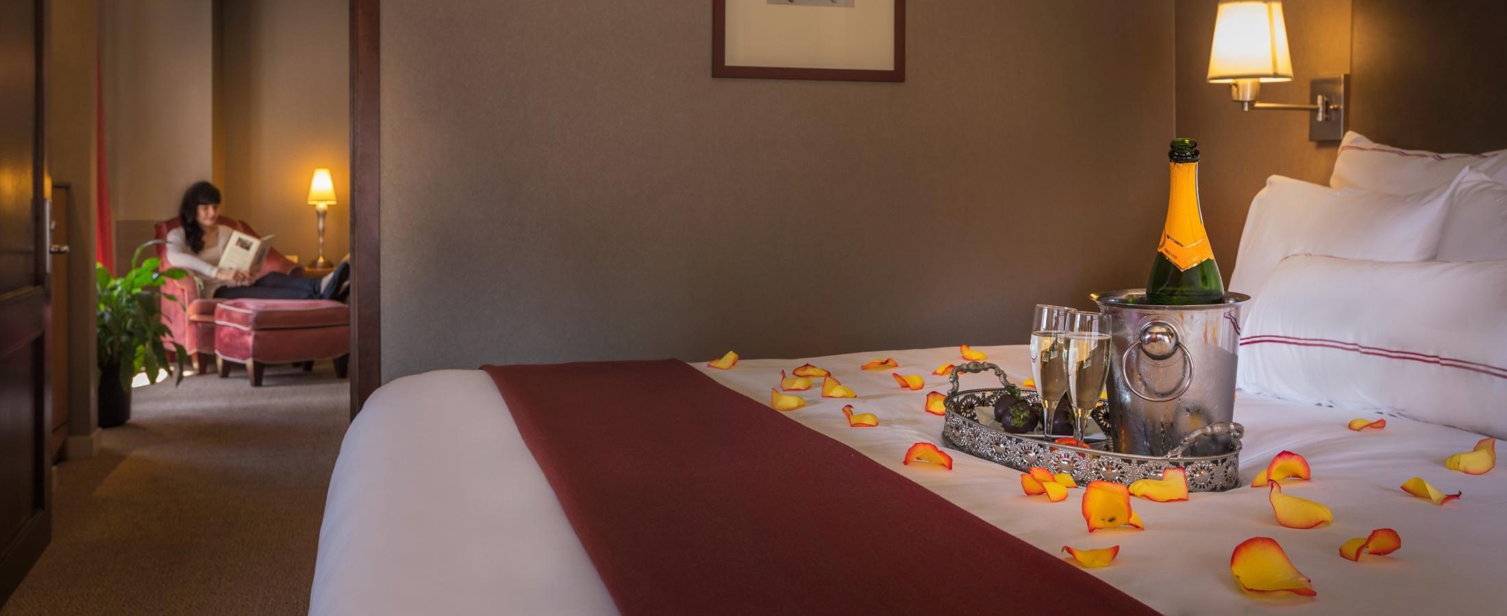 Rose petals, prosecco and chocolate strawberries set up on bed