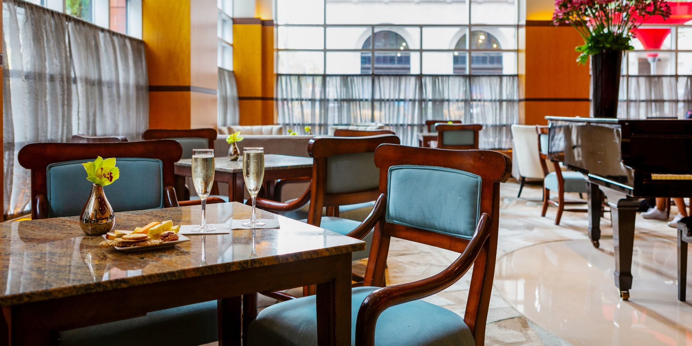 Grand Lobby with plenty of seating, tables, floor-to-ceiling windows, and a grand piano.